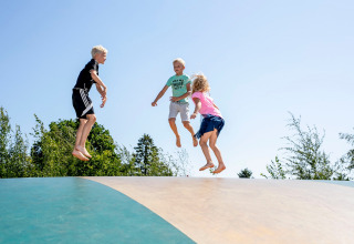 Kinderen springen samen op een grote luchtkussen in de open lucht bij een vakantiepark met glamping.