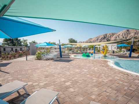 Espace piscine extérieure au Valamar Camping Baška avec transats, parasols et montagnes en arrière-plan.