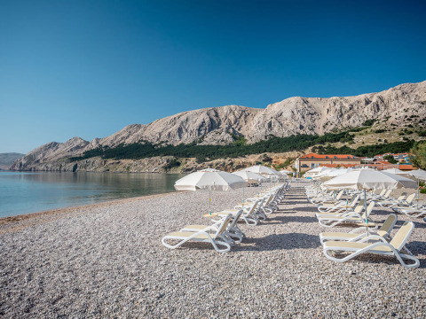 Plage avec transats et parasols à Valamar Camping Baška, entourée de montagnes en Primorje-Gorski Kotar, Croatie.