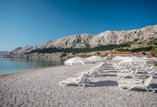Strand med liggestole og parasoller ved Valamar Camping Baška, omgivet af bjerge i Primorje-Gorski Kotar, Kroatien.