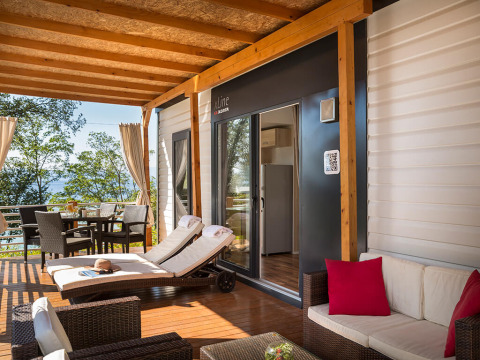 Terrazza coperta con lettini prendisole, tavolo da pranzo e divano in un villaggio vacanze croato sul mare.