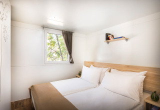Lichte slaapkamer met twee bedden, houten vloer en raam in Aminess Style Camping Atea Resort, Kroatië.