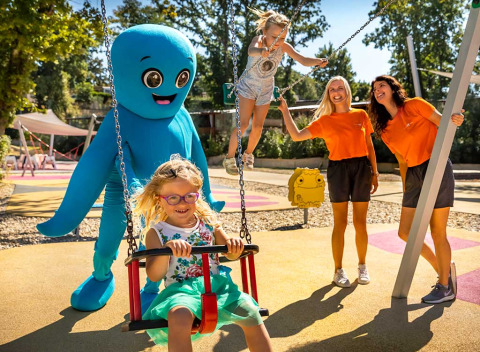 Bambini si divertono con una mascotte blu e lo staff al parco giochi di Aminess Style Camping Atea Resort in Croazia.