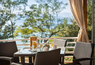 Outdoor dining area with wicker chairs and table, scenic sea and tree view at Aminess Style Camping Atea Resort.