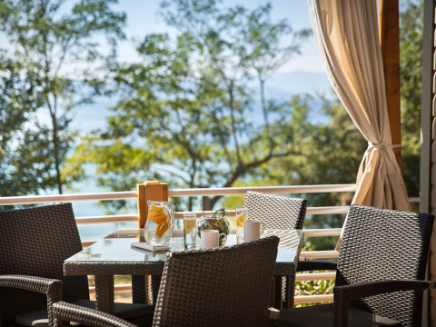 Outdoor dining area with wicker chairs and table, scenic sea and tree view at Aminess Style Camping Atea Resort.