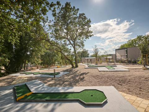 Parcours de mini-golf en plein air à Aminess Style Camping Atea Resort, entouré d’arbres et de cabanes modernes.