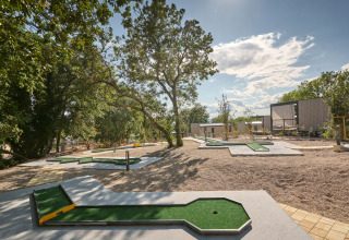 Campo de minigolf al aire libre en Aminess Style Camping Atea Resort, rodeado de árboles y modernas cabañas.