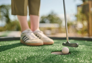Gros plan sur un joueur de mini-golf essayant de rentrer la balle dans le trou sous un soleil radieux.