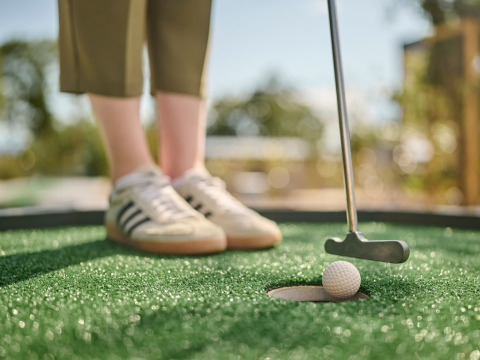Gros plan sur un joueur de mini-golf essayant de rentrer la balle dans le trou sous un soleil radieux.