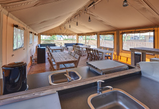 Ruime glampingtent met volledig uitgeruste keuken, houten tafels en stoelen bij vakantiepark Eigen Wijze.