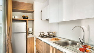Cocina moderna con gabinetes blancos, detalles en madera, estufa, fregadero y desayuno en la mesa.