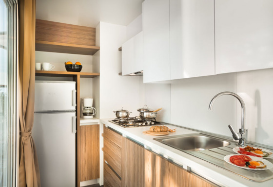 Cocina moderna con gabinetes blancos, detalles en madera, estufa, fregadero y desayuno en la mesa.