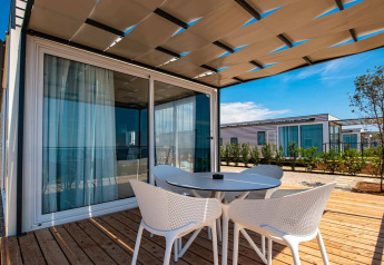 Udendørs terrasse ved chalet med bord og fire stole, trædæk og moderne skydedøre på en solrig dag.
