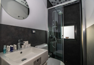 Moderne badeværelse i et chalet med glasbrusekabine, sort-hvide vægge, vask og toilet.