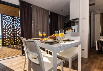 Moderne spiseområde i Camping Home Green chalet med appelsinjuice på bordet, Camping Arena Grand Kažela