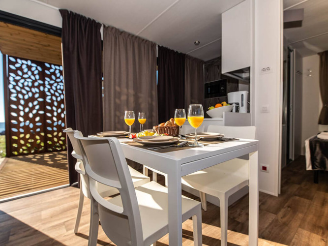 Moderne spiseområde i Camping Home Green chalet med appelsinjuice på bordet, Camping Arena Grand Kažela