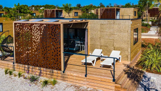 Modernes Chalet namens Camping Home Green mit Holzterrasse, Liegestühlen und stilvoller Verkleidung.
