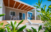 Modern chalet with sun loungers, wooden terrace, and greenery under a clear blue sky on a sunny day.