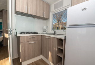 Modernes Chaletküche mit Holzschränken, Gaskochfeld, Spüle, Kühlschrank und Fenster mit Blick.