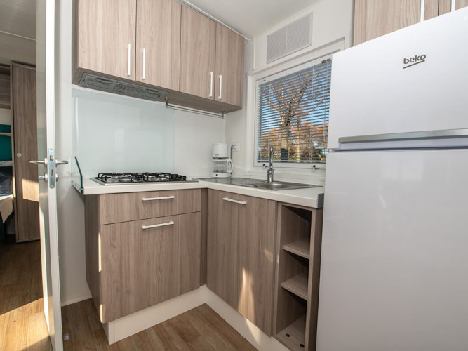 Moderne chaletkeuken met houten kasten, gaskookplaat, koffiezet, gootsteen, grote koelkast en raam.