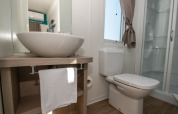 Salle de bain moderne de chalet avec vasque, miroir, toilettes, douche et lumière naturelle par la fenêtre.