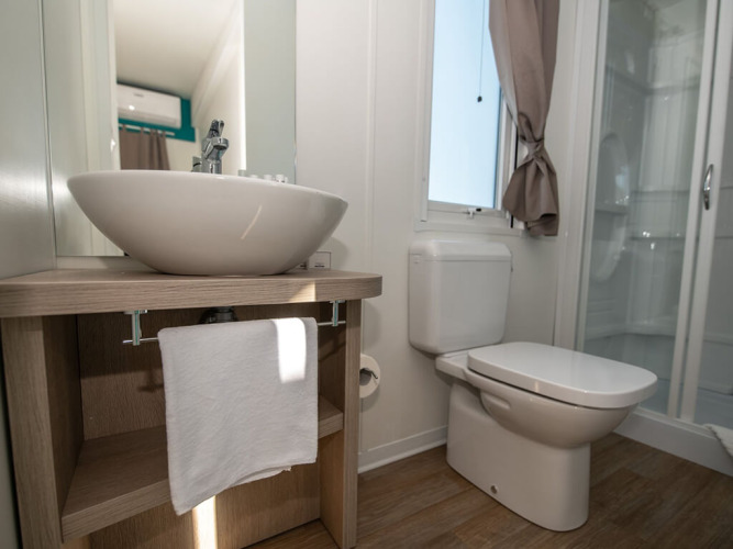 Bagno moderno di uno chalet con lavabo d’appoggio, specchio, wc, doccia e luce naturale dalla finestra.