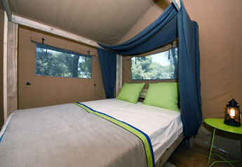 Interno di una tenda safari con letto matrimoniale e cuscini verdi al glamping Camping Arena Stoja, Croazia.