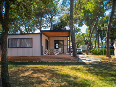 Deluxe Camping Villa Lodge mit moderner Veranda, umgeben von Bäumen und Wohnmobilen im Grünen.
