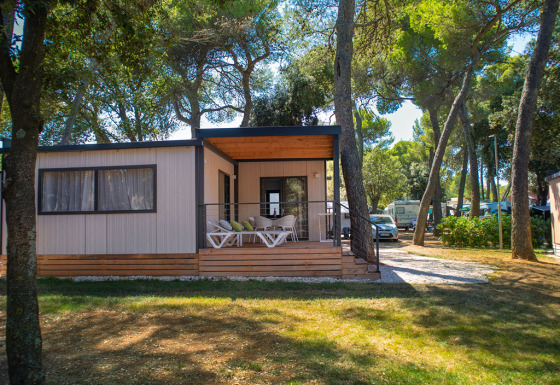 Deluxe Camping Villa Lodge mit moderner Veranda, umgeben von Bäumen und Wohnmobilen im Grünen.