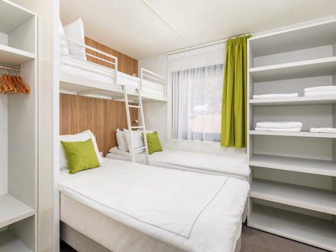 Modernes Camping-Villa-Zimmer mit Etagenbett, Einzelbetten, Regalen und grünen Kissen in Arena Stoja, Kroatien.