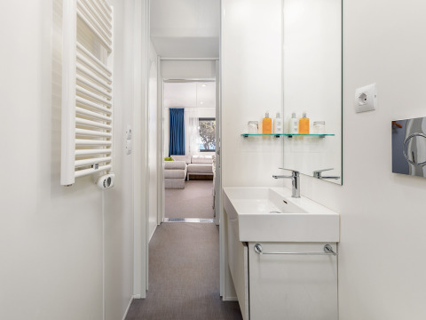 Bagno moderno con lavabo bianco, specchio e zona relax nella Deluxe Camping Villa First Row, Camping Arena Stoja.