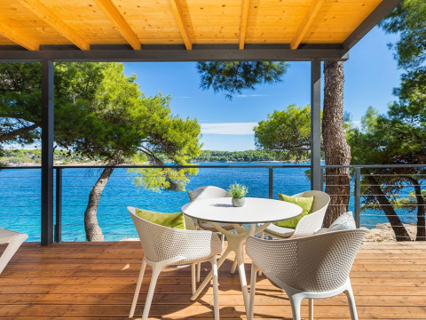 Terrazza in legno con tavolo e sedie, vista mare e pini al Camping Arena Stoja in Croazia.