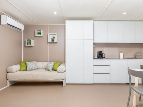 Moderne woonkamer en keuken in een chalet bij Camping Arena Stoja, Kroatië, met zetel en witte kasten.