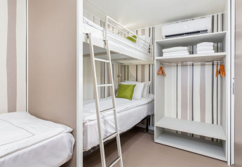 Modernes Chalet auf Camping Arena Stoja mit Etagenbett, offenem Kleiderschrank und frischer Bettwäsche.