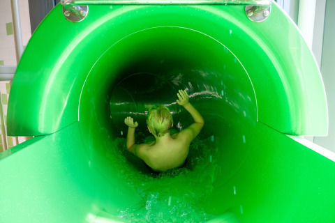 Een kind glijdt een groene waterglijbaan af in vakantiepark De Kleine Belties in Overijssel, Nederland.