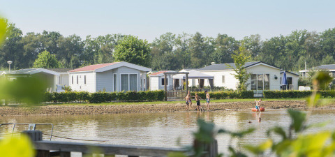 Kinderen spelen aan het water voor chalets in vakantiepark De Kleine Belties in het groene Overijssel.