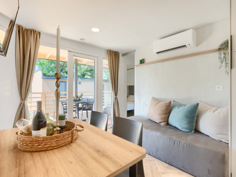 Modern lodge living room with a wooden table, wine, candles, sofa, pillows, and view of the terrace.