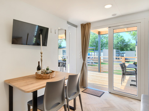 Modern lodge room with dining table, wall-mounted TV, large glass doors, and view of outdoor terrace.