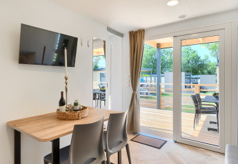 Intérieur de lodge moderne avec table à manger, TV murale, grandes portes vitrées et vue sur la terrasse.