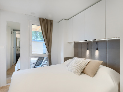 Chambre moderne de lodge avec literie blanche, rangements intégrés, lumière douce et fenêtre extérieure.
