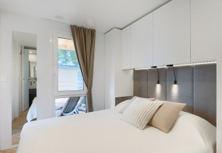 Modern lodge bedroom with white bedding, built-in cabinets, soft lighting, and a window view outside.