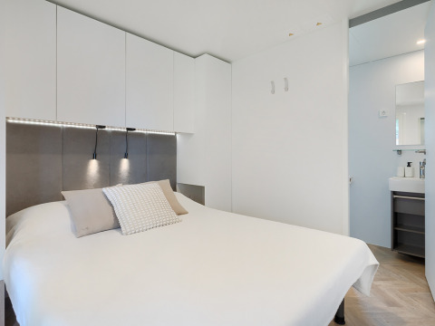 Chambre de lodge moderne avec déco blanche, lit double, rangements muraux et vue sur la salle de bain.