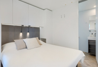Chambre de lodge moderne avec déco blanche, lit double, rangements muraux et vue sur la salle de bain.