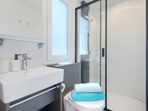 Salle de bain moderne en lodge avec douche, lavabo, toilettes et serviettes pliées, décor lumineux.
