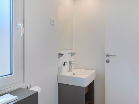 Salle de bain moderne dans un lodge avec lavabo blanc, miroir et fenêtre, au design minimaliste.