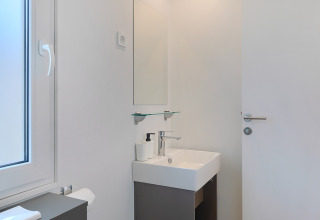 Modern lodge bathroom with a white sink, mirror, and window, featuring minimalist and clean decor.
