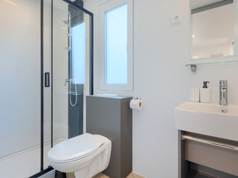 Modern, bright bathroom at a lodge featuring a shower, toilet, sink, and mirror with minimalist decor.