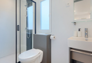 Salle de bain moderne et lumineuse dans un lodge, avec douche, toilettes, lavabo et miroir minimalistes.