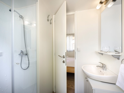 Baño moderno en el lodge San Marino Home con ducha, lavabo, espejo y vista hacia el dormitorio.