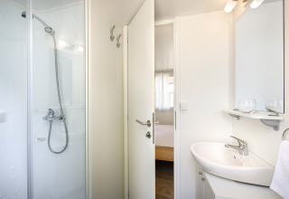 Baño moderno en el lodge San Marino Home con ducha, lavabo, espejo y vista hacia el dormitorio.
